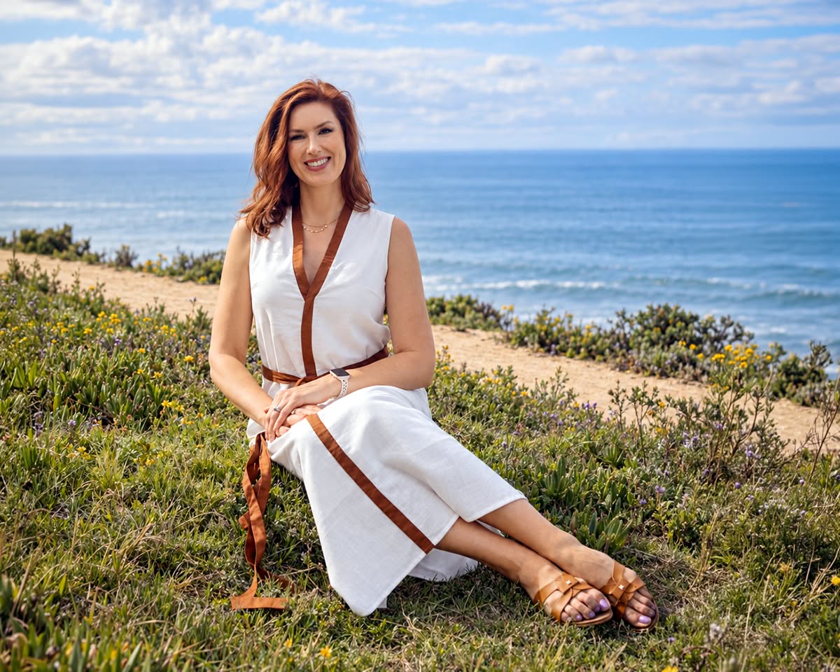 Ashley Hanna-Morgan, LCSW, PMH-C, seated among wildflowers on a coastal bluff above the ocean