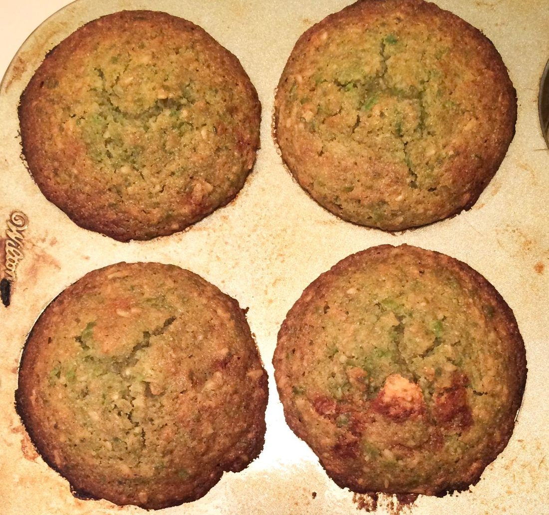 Four homemade sweet pea muffins, flecked with green, in a muffin tin.