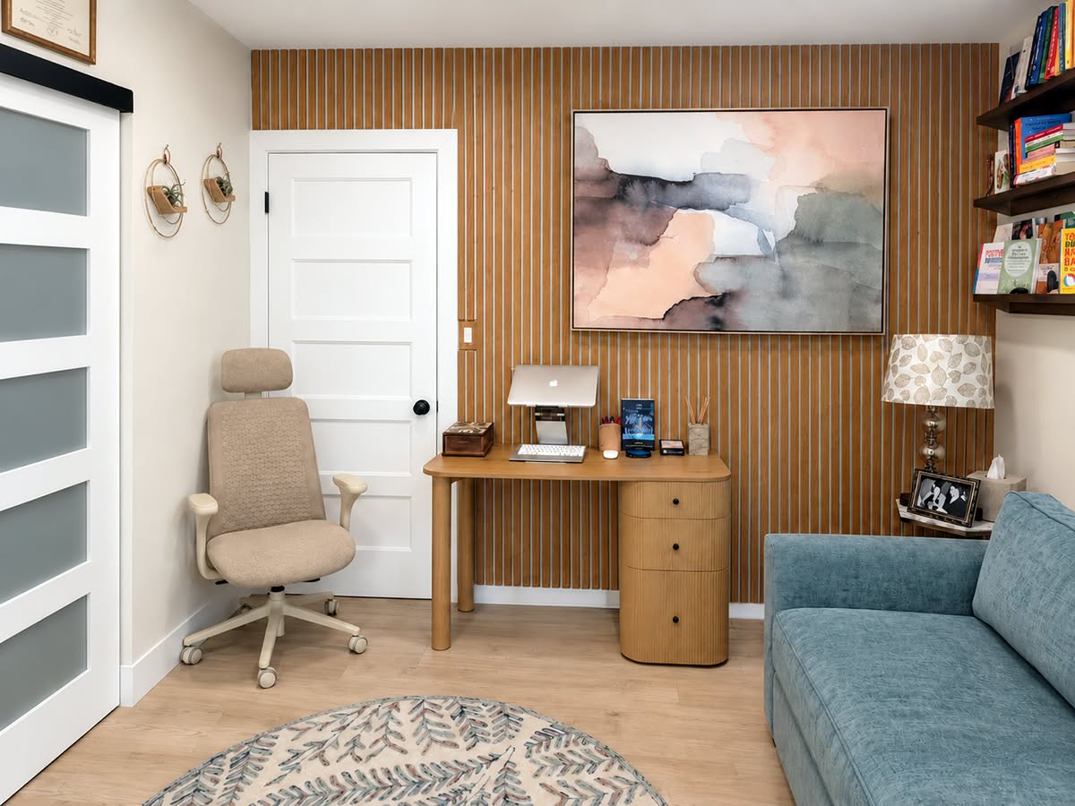 Ashley&rsquo;s therapy office: her chair and desk against a warm wood-slat wall, a watercolor painting above, and a soft blue couch